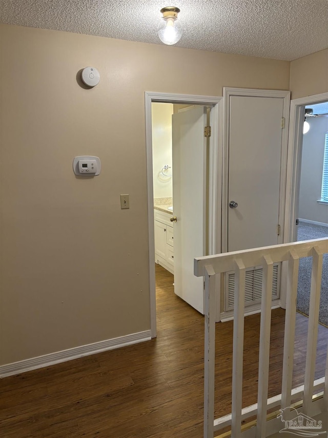 corridor featuring dark wood finished floors, visible vents, a textured ceiling, and baseboards