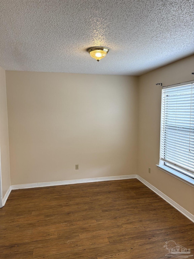 spare room featuring dark wood finished floors, a textured ceiling, and baseboards