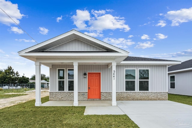 view of front facade featuring brick siding, a porch, a front yard, and board and batten siding