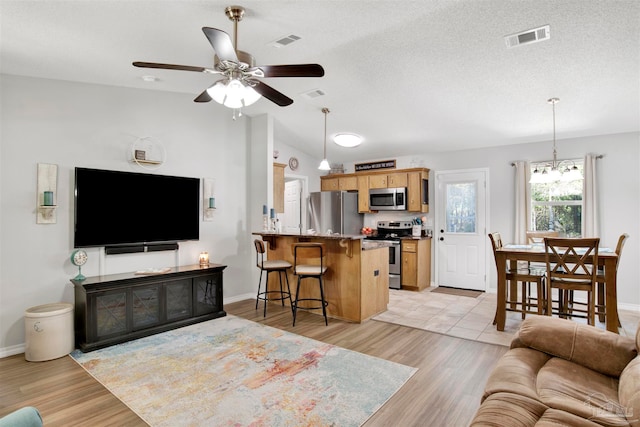 living room with a textured ceiling, light hardwood / wood-style floors, vaulted ceiling, and ceiling fan