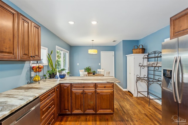 kitchen featuring dark wood-type flooring, kitchen peninsula, hanging light fixtures, appliances with stainless steel finishes, and light stone countertops