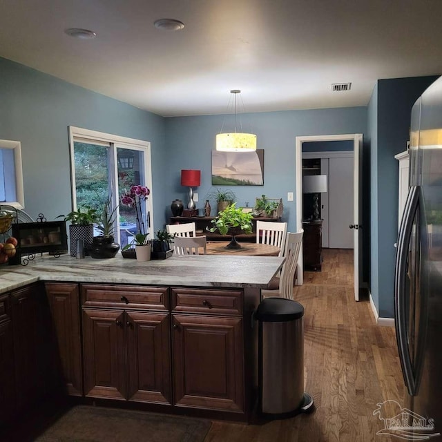 kitchen with dark brown cabinetry, hanging light fixtures, stainless steel fridge, and dark hardwood / wood-style flooring