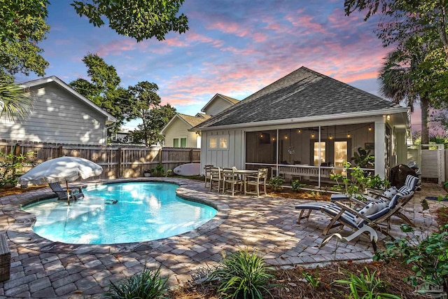 pool at dusk with a patio and a sunroom