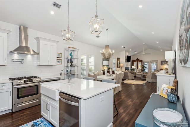 kitchen with dark hardwood / wood-style floors, stainless steel appliances, wall chimney exhaust hood, and a center island with sink