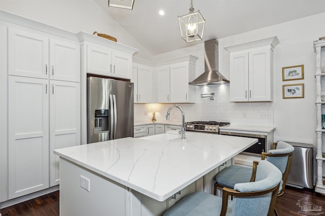 kitchen with appliances with stainless steel finishes, wall chimney exhaust hood, white cabinetry, and a kitchen island with sink