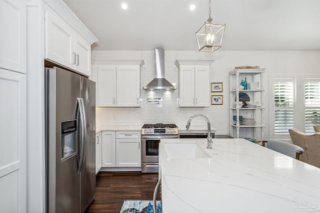 kitchen with hanging light fixtures, stainless steel appliances, wall chimney range hood, and white cabinets