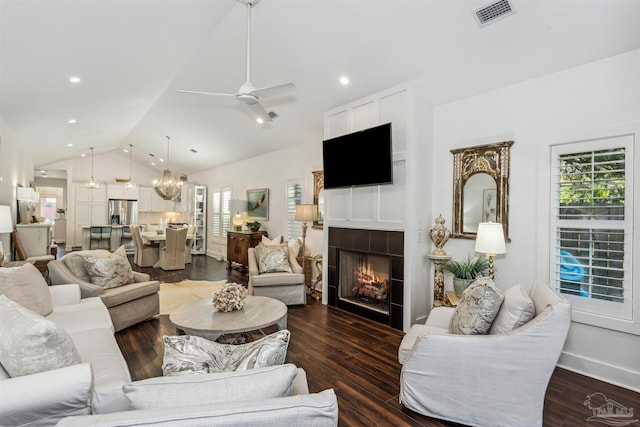 living room with dark hardwood / wood-style flooring, ceiling fan with notable chandelier, a fireplace, and vaulted ceiling