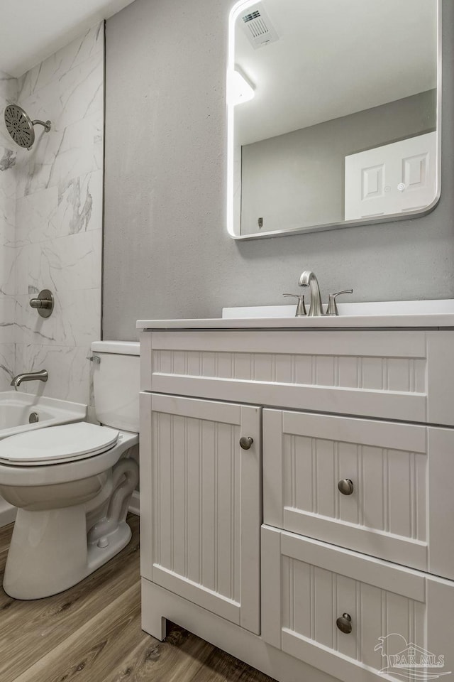 full bathroom with toilet, tiled shower / bath, vanity, and wood-type flooring