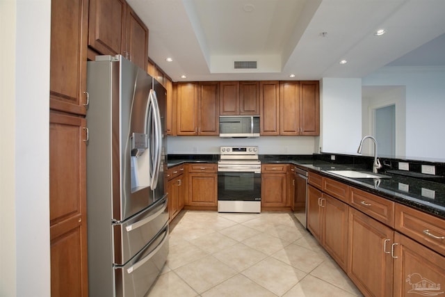 kitchen with light tile patterned flooring, sink, dark stone countertops, a tray ceiling, and stainless steel appliances