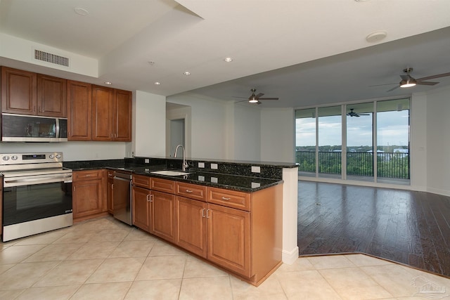 kitchen featuring sink, dark stone countertops, kitchen peninsula, stainless steel appliances, and floor to ceiling windows