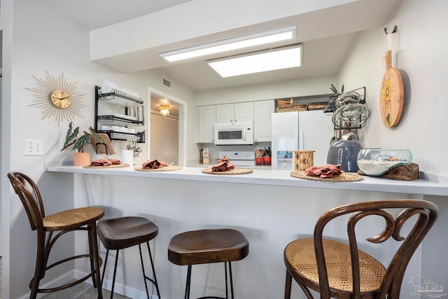 14259 Perdido Key Dr Unit 1C, Pensacola, FL 32507 - kitchen featuring white appliances, a breakfast bar, a peninsula, light countertops, and white cabinets