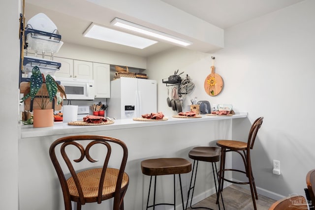 14259 Perdido Key Dr Unit 1C, Pensacola, FL 32507 - kitchen with a breakfast bar area, white cabinetry, light countertops, white appliances, and a peninsula
