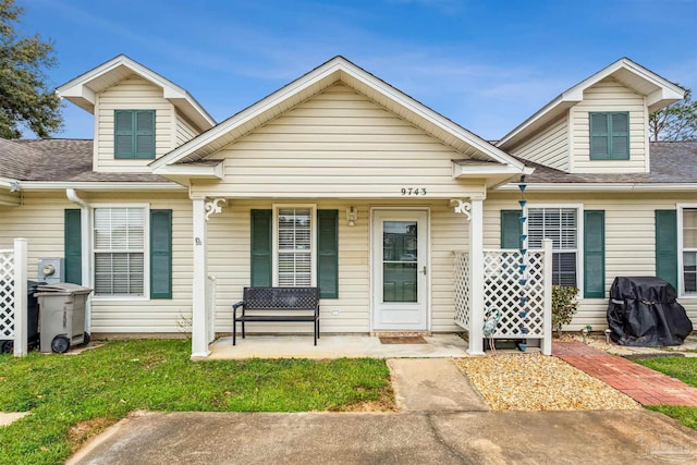 view of front facade with covered porch, a shingled roof, and a front yard