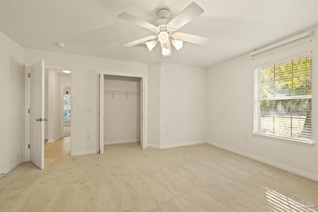 unfurnished bedroom featuring light carpet, a textured ceiling, a closet, and ceiling fan