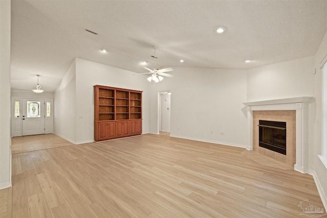 unfurnished living room with ceiling fan, built in features, light hardwood / wood-style flooring, lofted ceiling, and a tiled fireplace