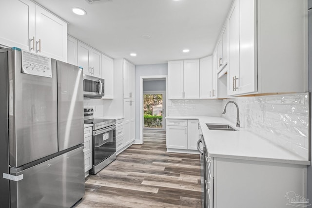 kitchen with white cabinetry, sink, stainless steel appliances, backsplash, and hardwood / wood-style flooring