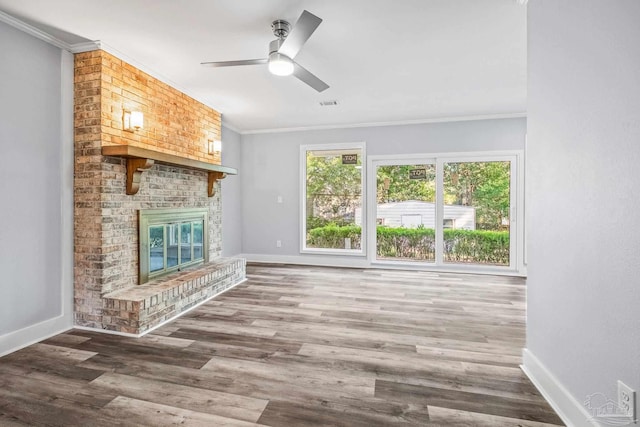 unfurnished living room with ceiling fan, wood-type flooring, ornamental molding, and a brick fireplace