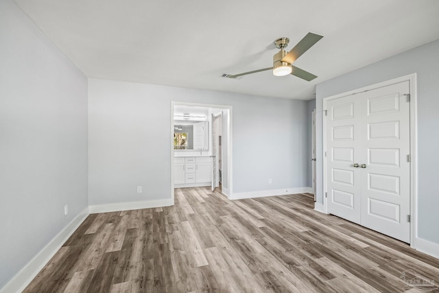 unfurnished bedroom featuring wood-type flooring, a closet, ensuite bathroom, and ceiling fan