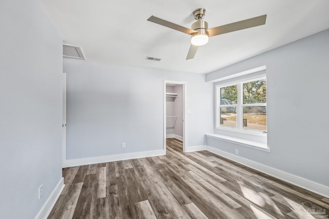 unfurnished bedroom featuring a closet, a walk in closet, hardwood / wood-style flooring, and ceiling fan