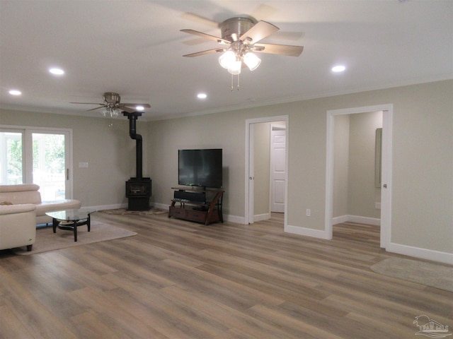 unfurnished living room with crown molding, ceiling fan, a wood stove, and hardwood / wood-style flooring