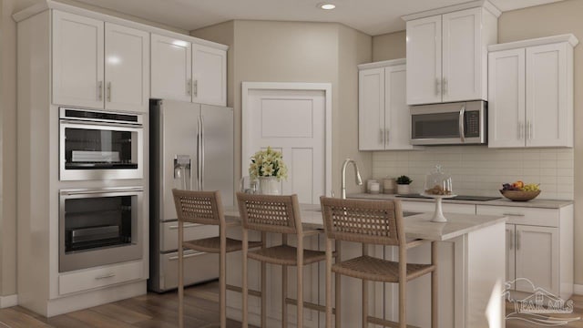 kitchen with a kitchen island with sink, stainless steel appliances, white cabinets, light countertops, and decorative backsplash