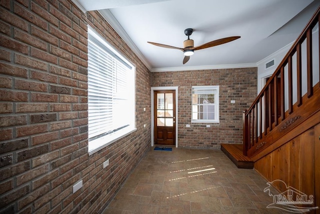 entrance foyer featuring ceiling fan, ornamental molding, and brick wall