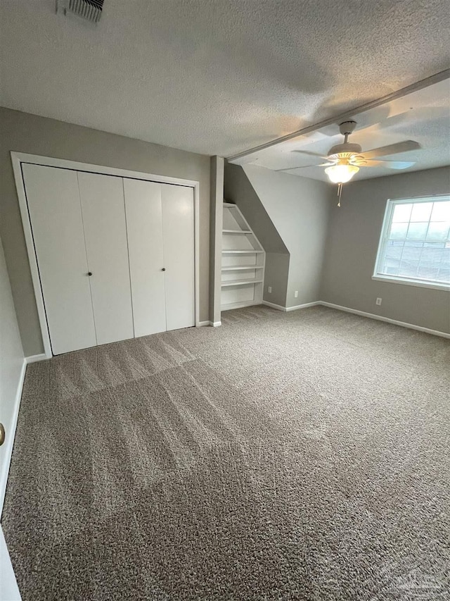 unfurnished bedroom with carpet flooring, a textured ceiling, a closet, baseboards, and ceiling fan