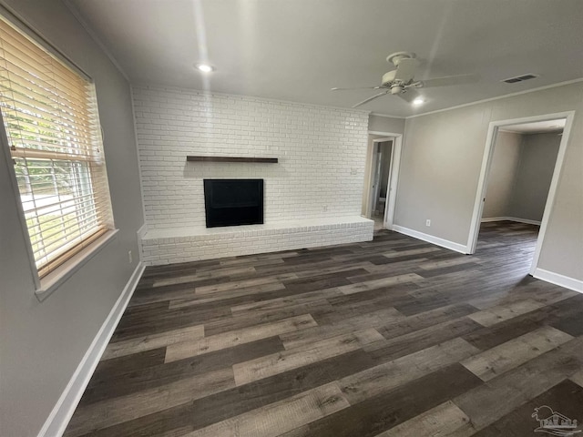 unfurnished living room featuring a brick fireplace, ceiling fan, baseboards, dark wood-type flooring, and crown molding