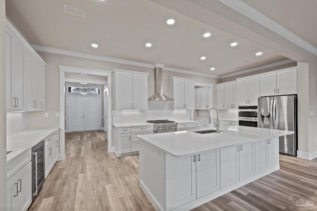 kitchen with sink, appliances with stainless steel finishes, an island with sink, white cabinets, and wall chimney exhaust hood