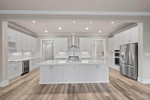 kitchen featuring appliances with stainless steel finishes, white cabinetry, an island with sink, wine cooler, and wall chimney exhaust hood