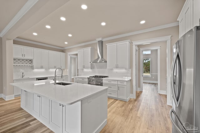 kitchen with sink, a kitchen island with sink, stainless steel appliances, white cabinets, and wall chimney exhaust hood