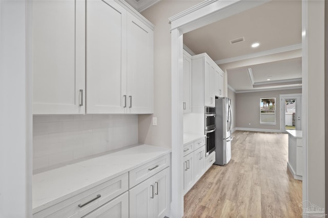 kitchen with white cabinetry, light stone counters, ornamental molding, appliances with stainless steel finishes, and a raised ceiling