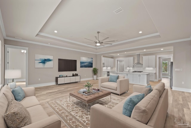 living room with crown molding, sink, light hardwood / wood-style floors, and a tray ceiling