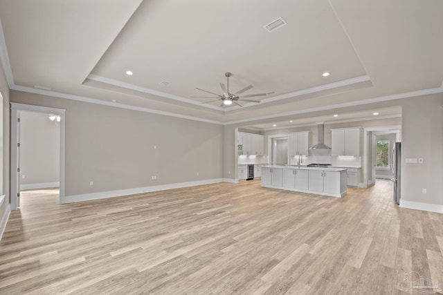 unfurnished living room with sink, light hardwood / wood-style flooring, a raised ceiling, and ceiling fan