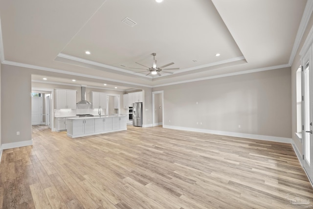 unfurnished living room featuring ceiling fan, ornamental molding, a tray ceiling, and light hardwood / wood-style flooring