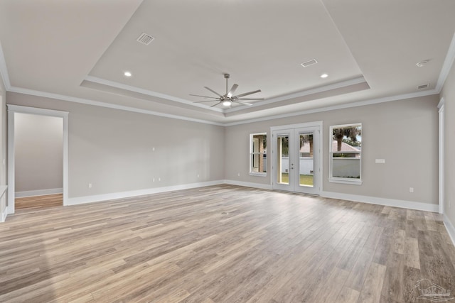 unfurnished living room with light hardwood / wood-style flooring, ceiling fan, a tray ceiling, ornamental molding, and french doors