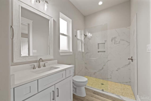 bathroom featuring hardwood / wood-style flooring, vanity, toilet, and a tile shower