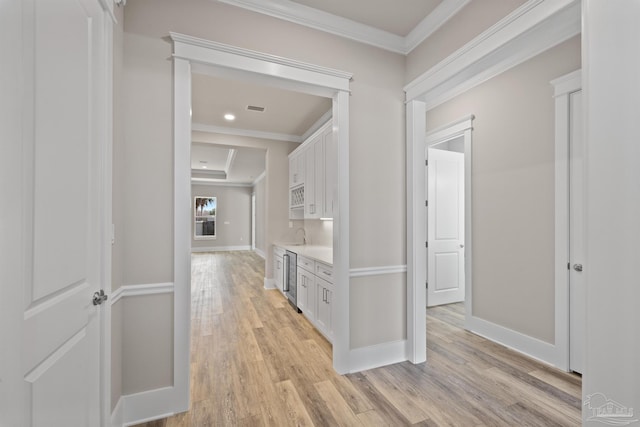 hallway with sink, ornamental molding, a raised ceiling, and light wood-type flooring