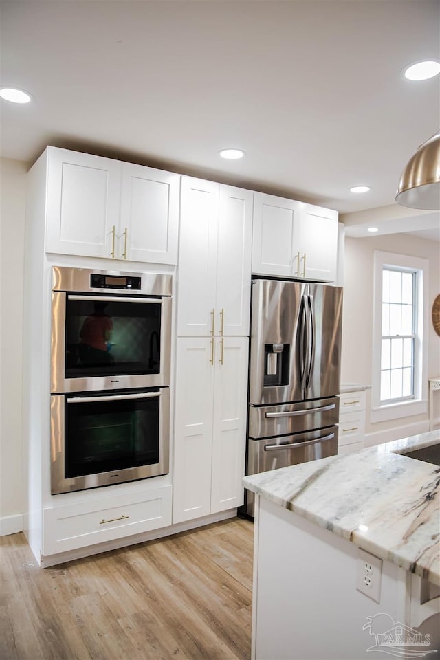 kitchen with light hardwood / wood-style floors, white cabinetry, light stone countertops, and stainless steel appliances