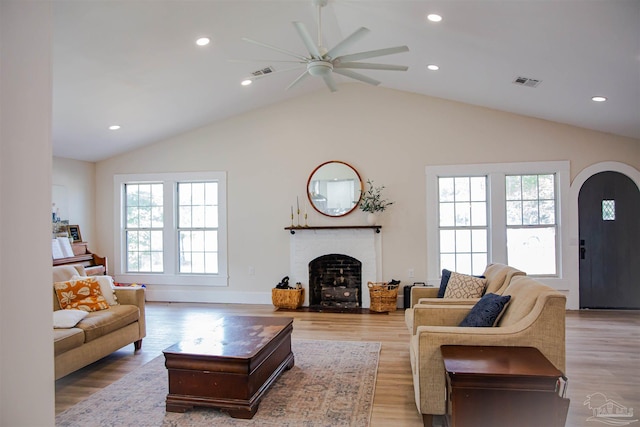 living room featuring a fireplace, light hardwood / wood-style flooring, ceiling fan, and vaulted ceiling