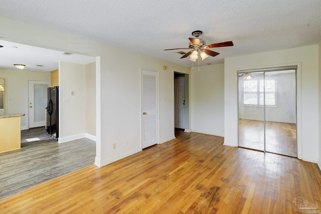 2007 E Gadsden St Unit 102, Pensacola, FL 32501 - unfurnished bedroom with light wood-type flooring, freestanding refrigerator, baseboards, a textured ceiling, and a ceiling fan