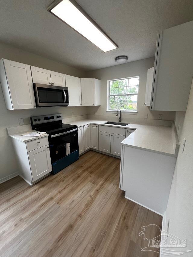 1984 Hillary Thompson Rd, Milton, FL 32570 - kitchen featuring range with electric stovetop, stainless steel microwave, a sink, light wood finished floors, and white cabinetry