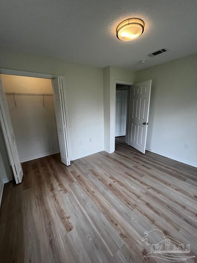 1984 Hillary Thompson Rd, Milton, FL 32570 - unfurnished bedroom with wood finished floors, baseboards, a closet, and a textured ceiling