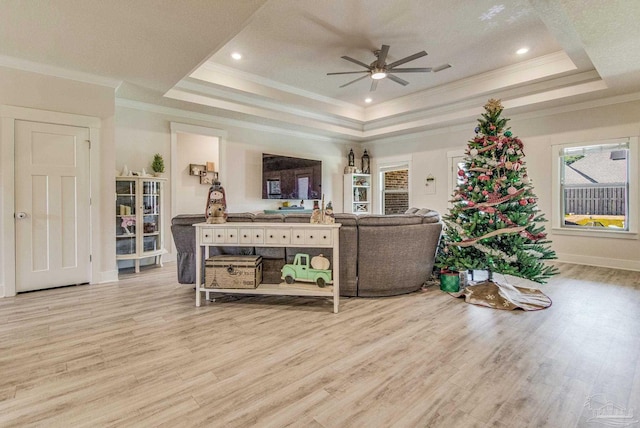 living room featuring a tray ceiling, crown molding, ceiling fan, and light wood-type flooring