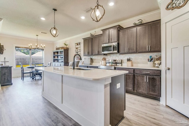 kitchen featuring sink, stainless steel appliances, pendant lighting, a kitchen island with sink, and ornamental molding