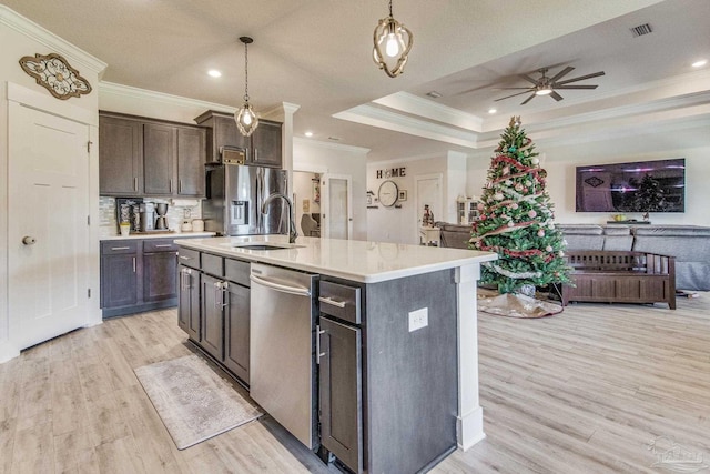 kitchen with hanging light fixtures, stainless steel appliances, light hardwood / wood-style floors, a kitchen island with sink, and ornamental molding