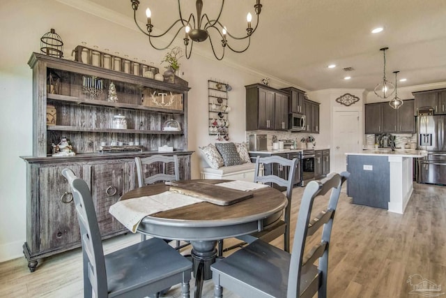 dining area with light hardwood / wood-style floors, ornamental molding, sink, and an inviting chandelier