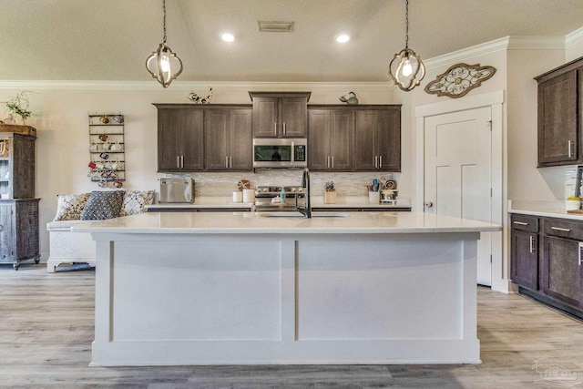 kitchen featuring sink, stainless steel appliances, an island with sink, pendant lighting, and light wood-type flooring