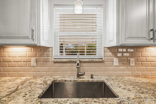 kitchen with tasteful backsplash, light stone counters, and a sink