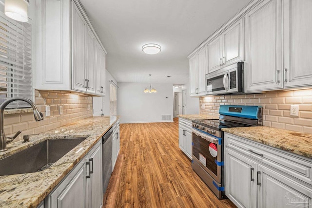 kitchen featuring light wood finished floors, stainless steel appliances, visible vents, white cabinets, and a sink